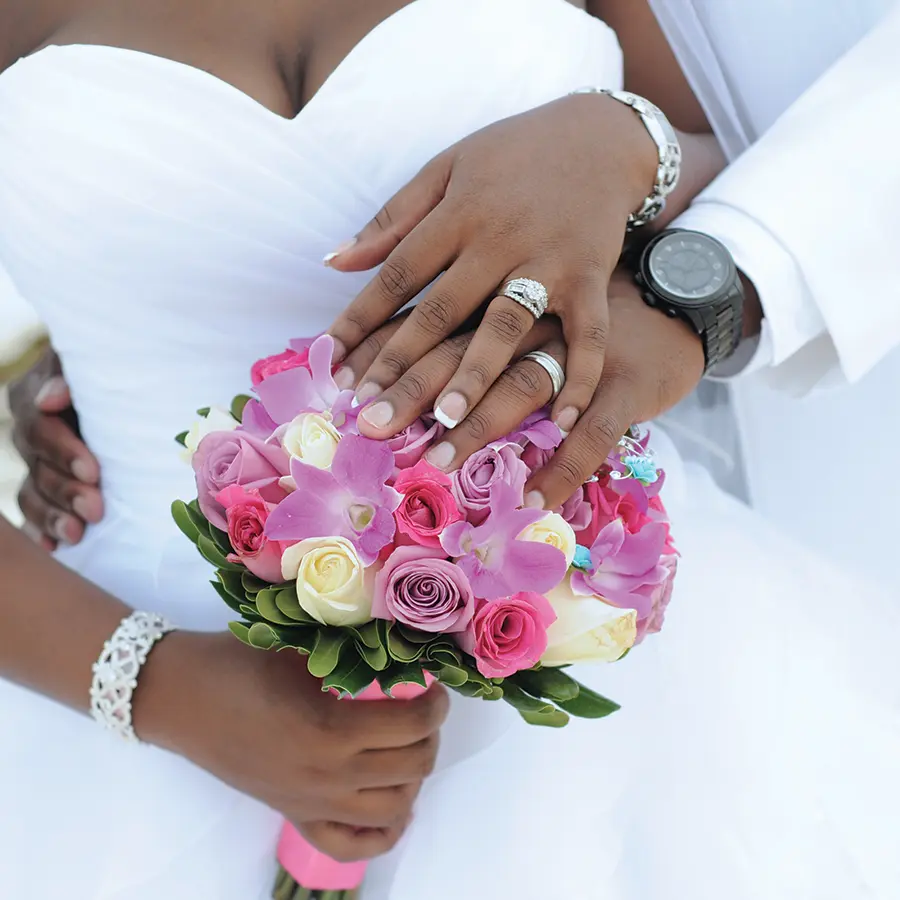 Bride and groom holding hands with pink and purple flowers.